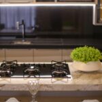Modern kitchen island with a four burner gas cooktop on a marble countertop and a green potted plant nearby