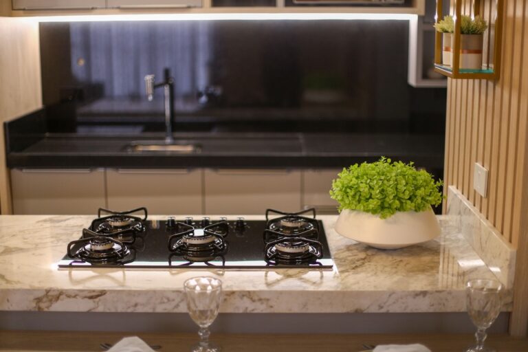 Modern kitchen island with a four burner gas cooktop on a marble countertop and a green potted plant nearby