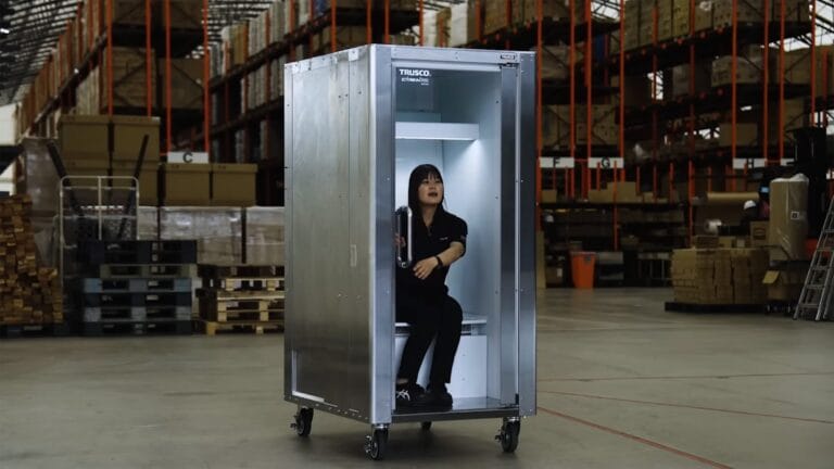 Woman sits inside a tall silver metal cabinet on wheels in a warehouse aisle