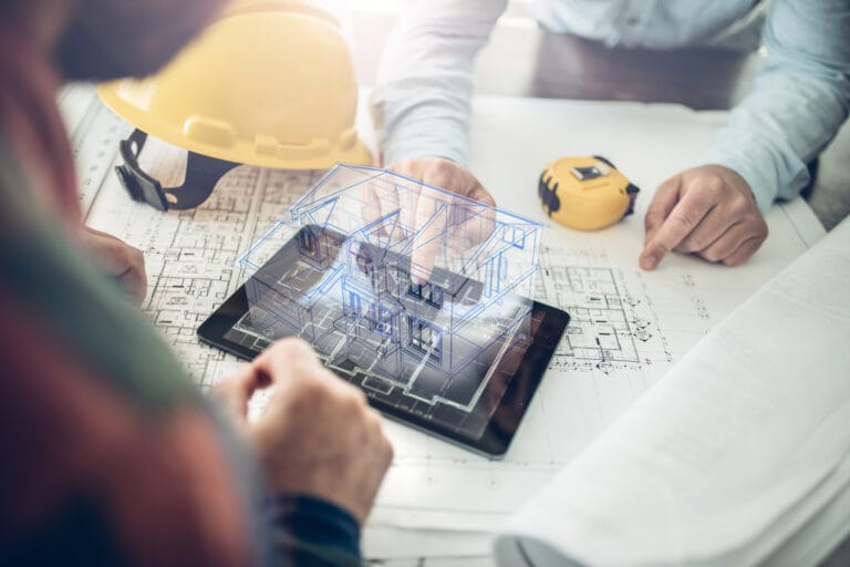 Engineers review blueprints on a drafting table with a yellow hard hat and a tablet showing a 3D building model