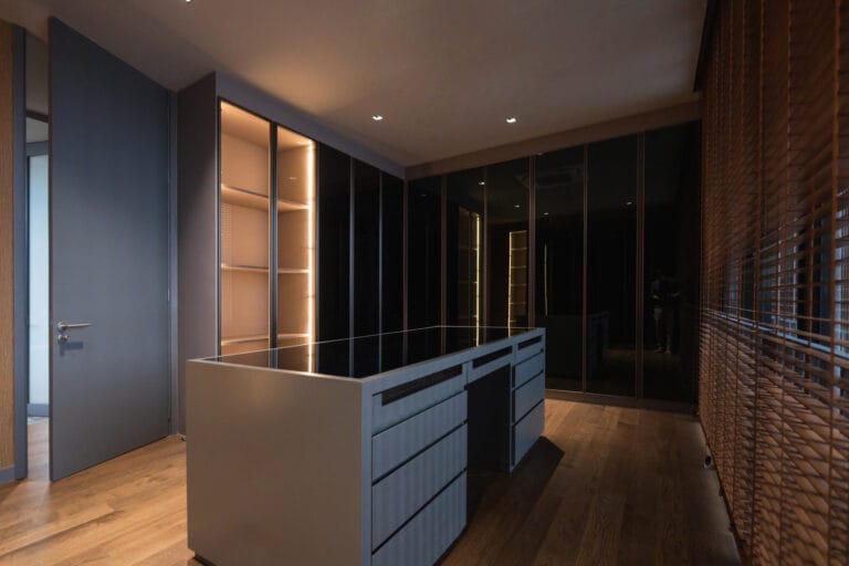 Modern interior with dark cabinets along a wall and a gray island in the foreground warm lighting and wood floors create a sleek contemporary showroom feel