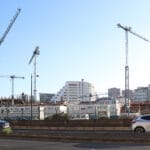 Construction site with tall cranes over under construction buildings against a clear blue sky