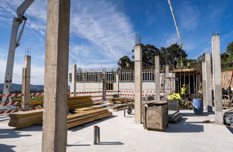 Construction site with vertical concrete columns lumber stacks and workers in safety gear under a blue sky