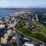 Aerial view of a coastal city with a star shaped fortress on a grassy hill amid modern buildings and a nearby harbor