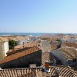 Panoramic view over terracotta rooftops toward the blue sea and clear sky