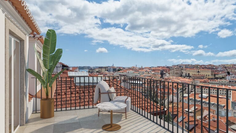 Balcony with a marble round table gray cushioned chair a tall potted plant and a city of red tiled roofs beyond the railing under a blue sky