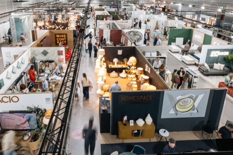Overhead view of a large furniture and home decor trade show with numerous booths lamps and display beds in a busy hall