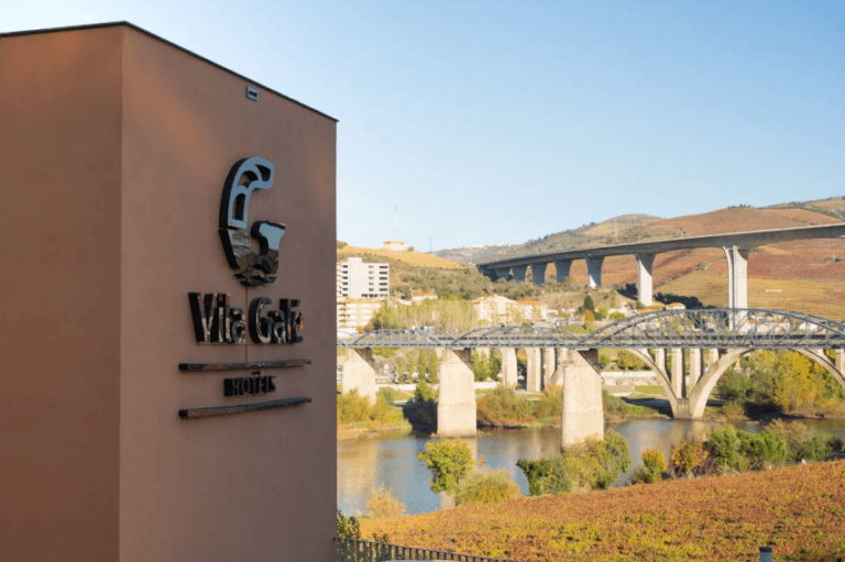 Vila Galé Hotels sign on a tan wall beside a river with several arched stone bridges and hills in the background