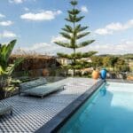 Poolside terrace with two striped lounge chairs lush plants and a clear blue pool under a sunny sky