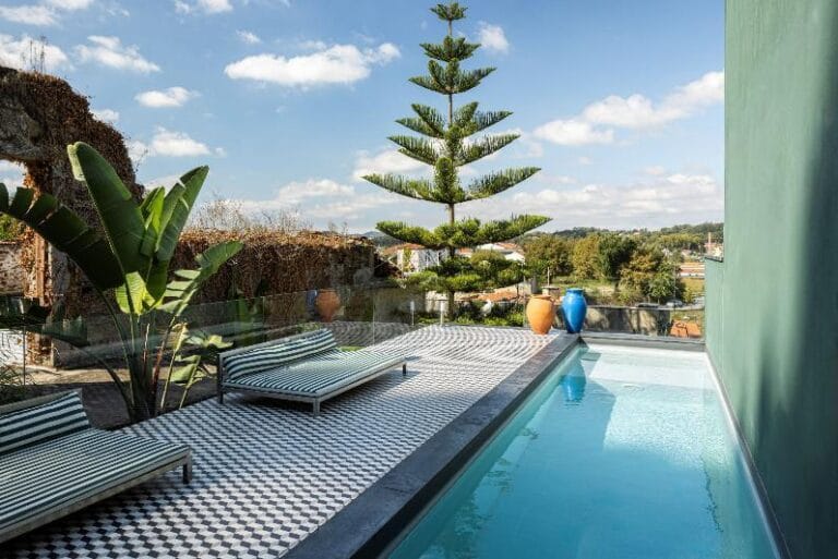 Poolside terrace with two striped lounge chairs lush plants and a clear blue pool under a sunny sky
