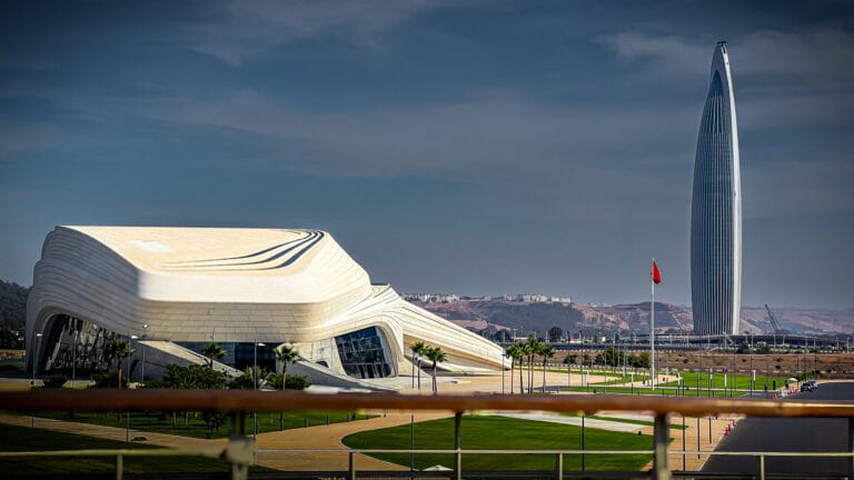 Futuristic white curved museum like building beside a tall slender glass skyscraper under a blue sky