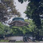 Ornate wrought iron gazebo with a teal roof in a green park surrounded by trees