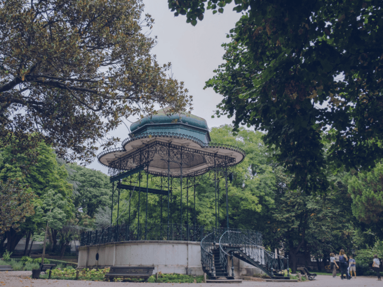 Ornate wrought iron gazebo with a teal roof in a green park surrounded by trees