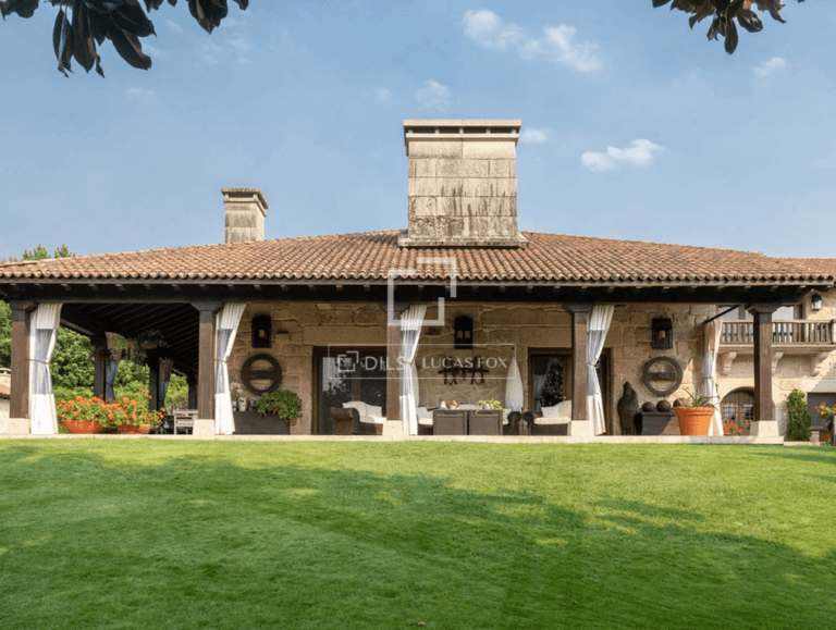 Rustic stone house with a wide covered patio and white curtains outdoor seating and a green lawn in front