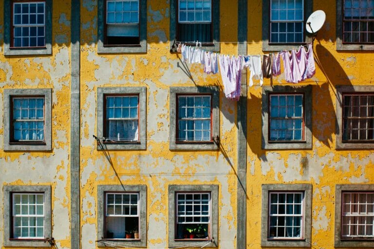Weathered yellow apartment building with peeling plaster gray framed windows laundry hanging on a clothesline across the facade and a satellite dish on the right side