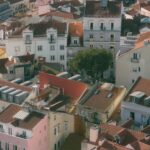 Aerial view of a dense hillside neighborhood with pastel buildings and red tiled roofs and a cluster of trees in the center of the block