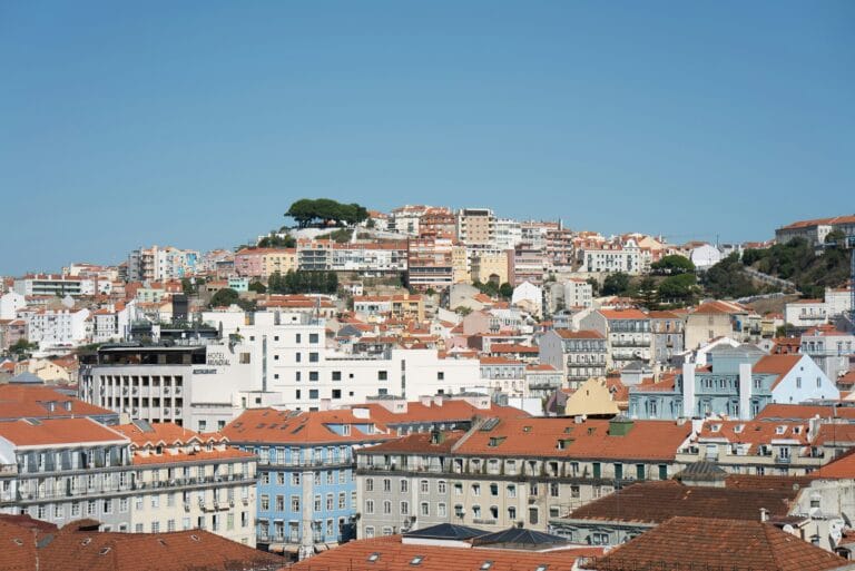City hillside with densely packed buildings and orange roofs under a clear blue sky