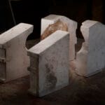 Four pale concrete blocks arranged in a rough circle on a dusty workshop floor with a brown clay like lump in the center