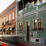 Colorful street scene with pastel storefronts green building with wrought iron balconies and light trail traffic