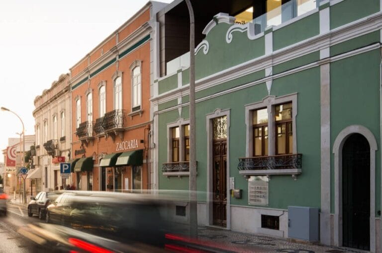 Colorful street scene with pastel storefronts green building with wrought iron balconies and light trail traffic