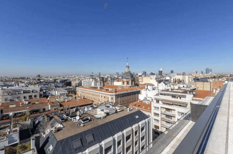 City skyline seen from a rooftop with red tiled roofs a domed central building and a clear blue sky above
