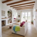 Bright living room with white walls exposed wooden ceiling beams and large windows colorful throws on a white sofa on the right side