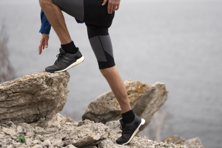 Climbers feet in black athletic shoes step along jagged rocks with a calm body of water in the background