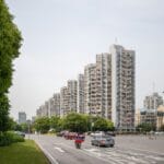 Tree lined city street with tall residential buildings on the right and several cars in the road
