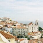 Coastal town with white buildings and red tiled roofs a large domed church on the left and the sea in the distance under a blue sky