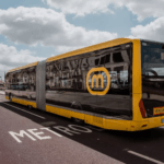 Articulated yellow and black bus with a circular M logo on its side parked on a street with a large METRO marking on the road