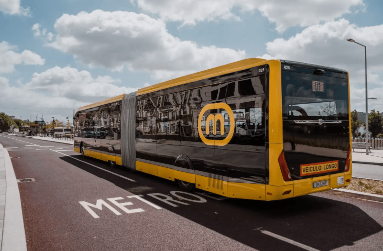 Articulated yellow and black bus with a circular M logo on its side parked on a street with a large METRO marking on the road