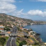 Coastal hillside town with orange roofed houses overlooking a winding highway along the shore