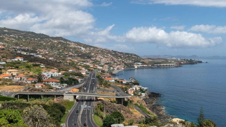 Coastal hillside town with orange roofed houses overlooking a winding highway along the shore
