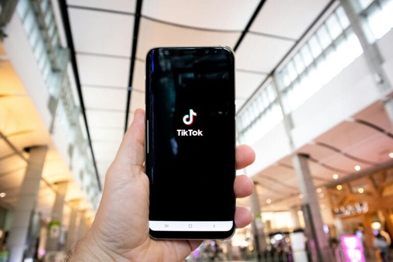 Hand holding a smartphone displaying the TikTok logo in a bright indoor mall atrium