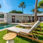 Modern backyard with a rectangular pool wooden lounge chairs and a white house with glass doors