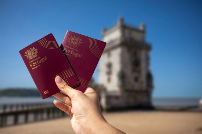 Two red Portugal passports held up in the foreground with a blurred seaside fortress in the background