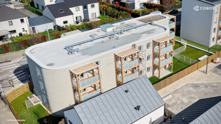 Aerial view of a curved modern apartment building with wooden framed balconies and a flat rooftop with pipes and vents