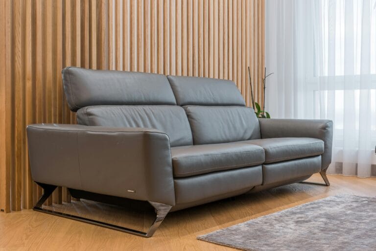 Gray leather sofa with metal legs beside a vertical wooden slat wall in a bright living room