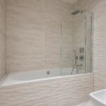 Beige tiled bathroom with a built in tub and a glass shower enclosure on the right