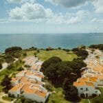Aerial view of a seaside village with white houses and orange tiled roofs along green cliffs overlooking the blue ocean