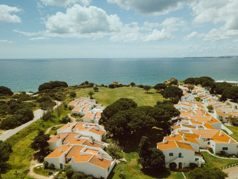 Aerial view of a seaside village with white houses and orange tiled roofs along green cliffs overlooking the blue ocean