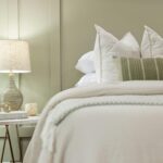 Bedside table scene woven lamp round marble table and decorative items beside a neatly made bed with white pillows and a green striped throw rack