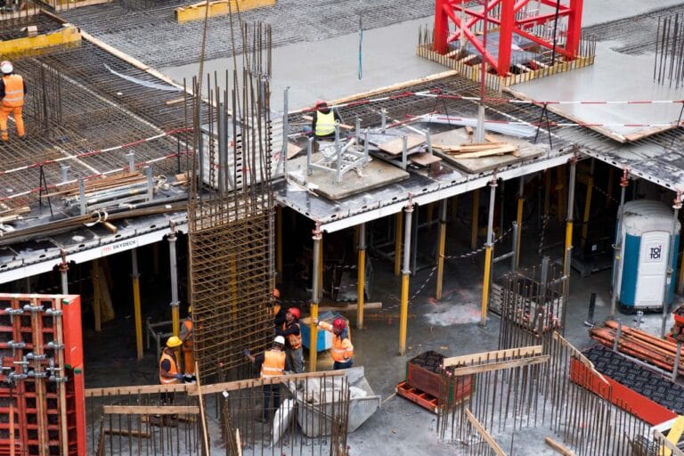 Construction site with workers in orange vests and hard hats assembling steel reinforcement framework for a building