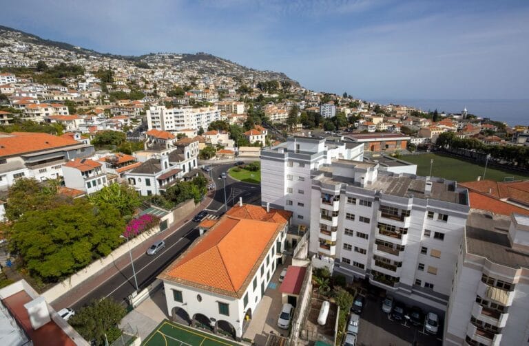 Aerial view of a coastal town with white buildings and orange roofs on a hillside the sea visible in the distance