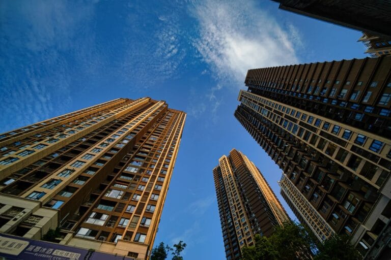 Tall residential skyscrapers seen from the ground looking up at a bright blue sky between buildings from a street level perspective