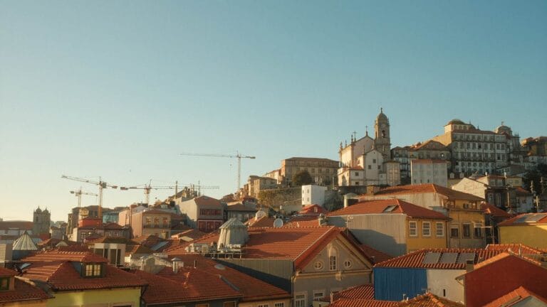 Sunlit hillside cityscape with red tiled rooftops a church tower and construction cranes in the distance