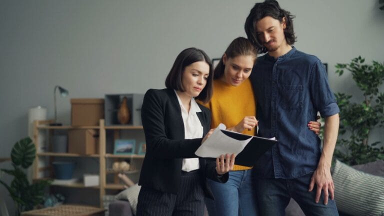 Professional woman in a blazer explains documents to a couple in a casual living room setting