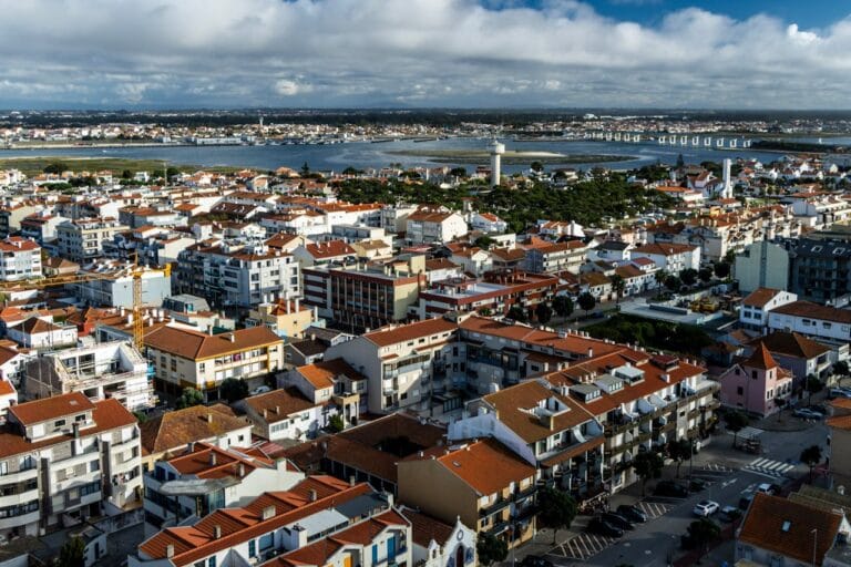 Aerial view of a coastal town with red tiled rooftops and a river in the distance under cloudy skies