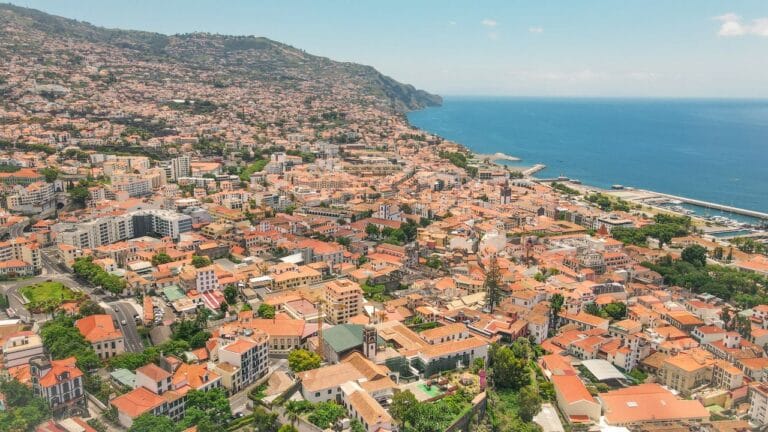 Aerial view of a coastal town with orange tiled roofs hillside housing and blue sea to the right