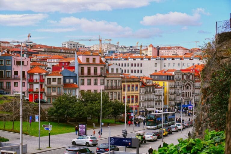 Colorful row of pastel buildings on a hillside with a busy street and a blue bus in the foreground